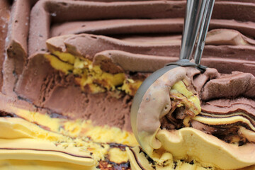 Scoop ice creame process. Textured orange and chocolate ice cream in a plastic box on white background with copy space. Selective focus
