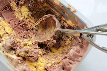 Scoop ice creame process. Textured orange and chocolate ice cream in a plastic box on white background with copy space. Selective focus
