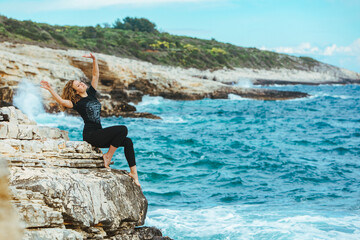 young slim woman sitting on the cliff edge looking at sea