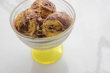 Scoops of orange and chocolate ice cream in a glass dessert bowl on white background with copy space. Selective focus

