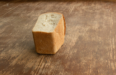 Half a loaf of bread lies on an old wooden table. The concept of poverty, malnutrition