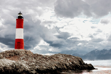 Les Eclaireurs lighthouse on a stone island near Ushuaia (Argentina) with cloudy sky and mountains in the background