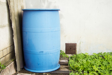 A large blue plastic rainwater barrel stands outside near the wall. It is used for watering.