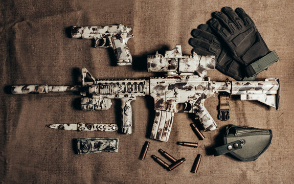 AR-15 camouflaged rifle laying on table with tactical gear.