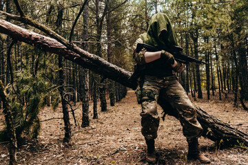 Forest sniper in camouflage and tactical ammunition standing with rifle.