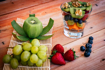 A glass cup with healthy fresh colorful fruit salad ready to eat. Wooden background with kiwi grapes strawberry and blueberries