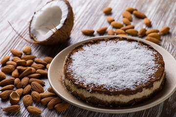 Diet cake with cocoa and coconut on a beige plate on a white wooden table against the background of almonds and broken coconut