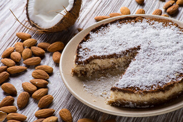 Diet cake with cocoa and coconut on a beige plate on a white wooden table against the background of almonds and broken coconut