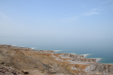 Fototapeta na wymiar Dead Sea coast on the Jordanian side with salt deposits and bright blue water on a warm spring day, Dead Sea, Jordan