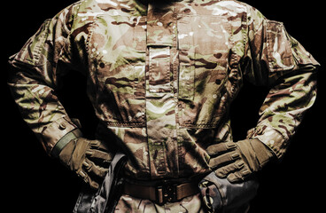 Soldier in multi camouflaged tunic clothing and tactical belt standing on black background. - obrazy, fototapety, plakaty