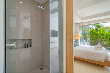 Interior design of shower room ensuite in bedroom in luxury villa feature shower head, sliding door joining to bedroom, bedding, towels on bed amd pool view