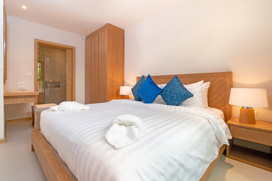 Interior design of bedroom in luxury villa, apartment feature bed, beding, duvet, towels, cushion, bedside table lamp and sluding door with garden view