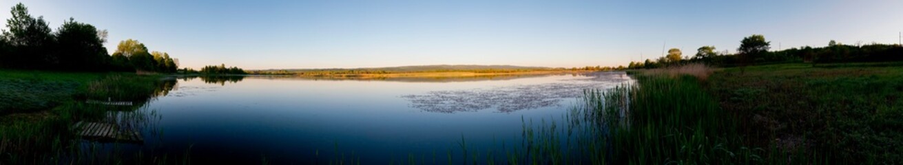 Panoramic landscape from the lake shore with colorful clouds in the spring sun.