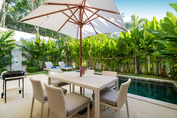 Exterior design in luxury pool villa feature pool terrace, garden landscape, outdoor dining table, BBQ, dining chair and umbrella overlooking to living room