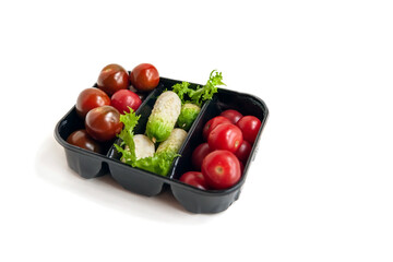 Fresh ripe little cocktail cucumbers and cherry tomatoes in a plastic black container. Isolated on white, copy space