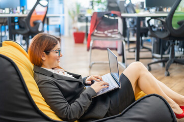 Business woman sits in a cozy chair bag and typing on a laptop. Female Manager works in a modern office. Caring for the convenience of employees. beanbag in the workplace.