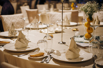 Decorated banquet tables for guests at wedding, on table plates, knives, forks, wine glasses, napkins, flowers and lemons