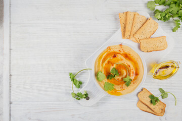 Healthy snack from crispbread with hummus, olive oil and cillantro on white wooden background.