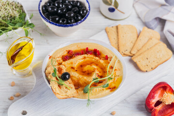 A bowl of chickpeas homemade hummus with olive oil, crispbread, microgreen and smoked paprika on white wooden background