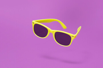 Yellow sunglasses floating above a purple background with a centre composition