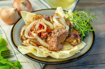 Beshbarmak dish: noodles with lamb and onion close-up on a plate on the table