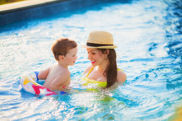 beautiful mother in a yellow bathing suit and hat swims in the pool with her son in a rubber ring