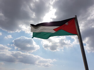 The flag of Jordan is waving in the wind in the front of a cloudy sky in the ruins of Umm Qais, Jordan