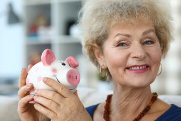 Happy elderly woman in apartment shows piggy bank
