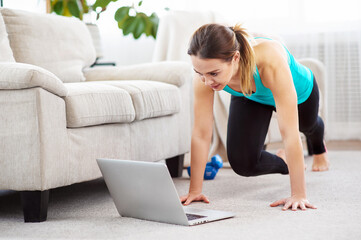 Online home fitness. Slim girl doing workout routine on floor and watching laptop at home. Copy...