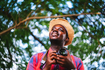 Happy african man traveler on vacation photographing with a dslr camera on the green nature background