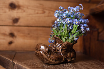 Ceramic shoe with a bouquet of forget-me-nots. On a wooden background.