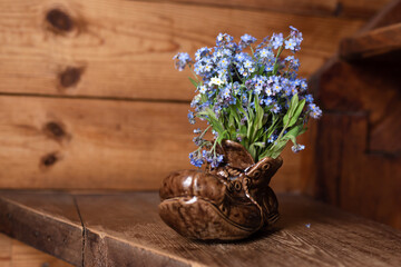 Ceramic shoe with a bouquet of forget-me-nots. On a wooden background.