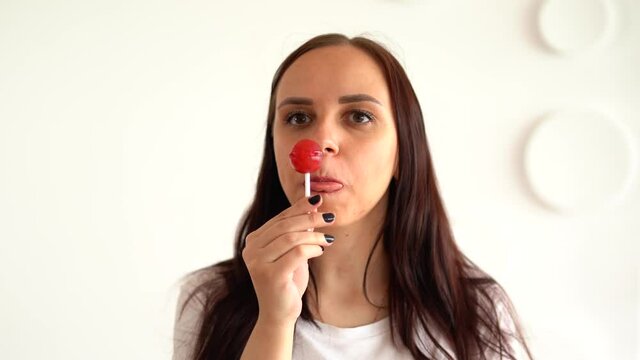 Young woman licking big lollipop against white patterned wall. Close up of adult female eats candy on stick.