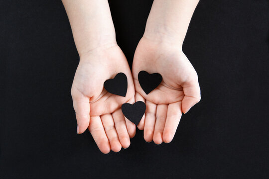 White Human Hands Holding Black Paper Hearts On Dark Background. Person Support Activist Of USA Movement Black Lives Matter. People Protest Against Racism. Blackout Tuesday, 2020.