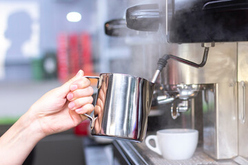 Coffee shop worker preparing coffee on steam espresso coffee machine. Barista Warming Milk In Metal Jug With Steam Of Coffee Machine
