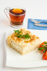 Traditional Turkish Cheesy Water Patty on the white porcelain plate with tomato slices,cutlery set and a cup of tea.