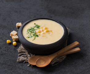 Corn cream soup in a wooden bowl on a linen napkin in rustic style on a dark gray background 