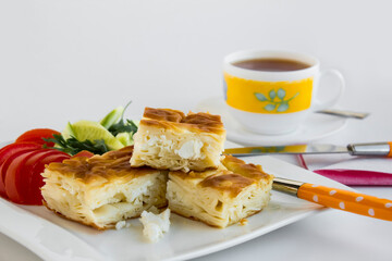 Traditional Turkish Cheesy Water Patty on the white porcelain plate with tomato slices,cutlery set and a cup of tea.