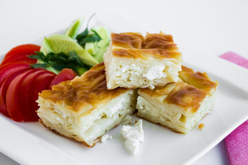 Traditional Turkish Cheesy Water Patty on the white porcelain plate with tomato slices,cutlery set 