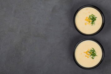 Corn cream soup with oatmeal cream in a bowl on a dark gray background 
top view copy space