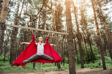 Young woman doing twine in a hammock for yoga, exercising in nature.