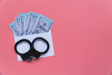 close up handcuffs with money in an envelope on a pink background