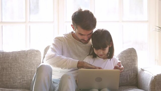 Caring and patient father teaches little daughter how computer works family spend free time sit on sofa, elder brother helps younger sister understand modern device and virtual entertainment concept