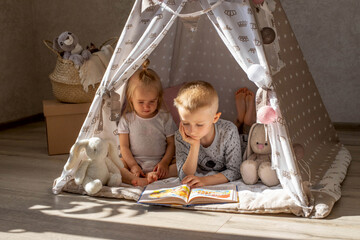 Children brother and sister in the tent play, read a book.