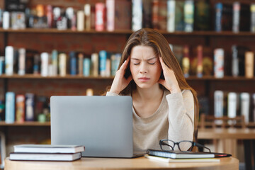 Tortured young woman trying to focus on working on laptop
