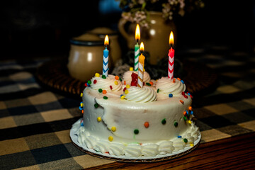 white birthday cake with burning candles isolated on wood table with blue table cloth