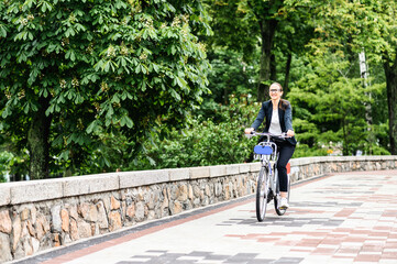 Obraz premium Alternative transport to get for work. Young woman in formal wear is riding a bicycle to the office on the city street