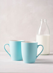 Two blue mugs and a bottle of milk are standing on a gray concrete table. Vertical orientation, there is a copy space.