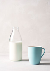 Milk in a glass bottle with a blue mug stands on a gray concrete table. Vertical orientation, there is copy space.