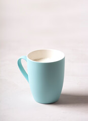 A blue mug with milk stands on a gray concrete table. Side view, vertical orientation. There is copy space.